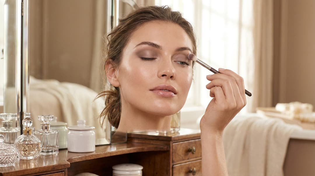 Beautiful woman applying matte eyeshadow slightly above the crease on hooded eyes in soft light