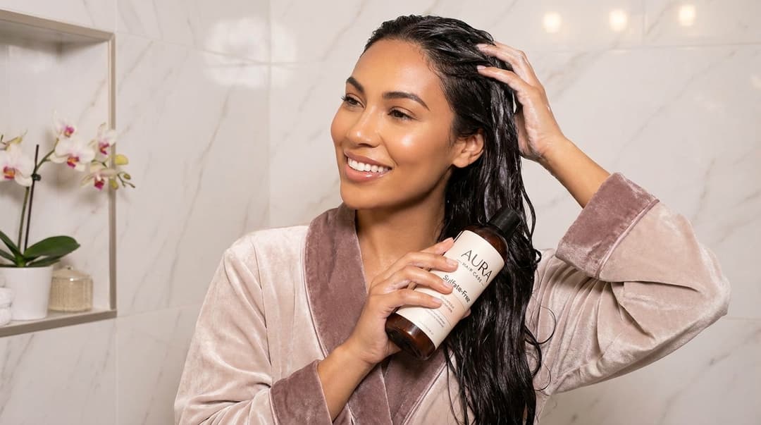 Beautiful woman with shiny color-treated hair using shampoo in a bright luxury shower