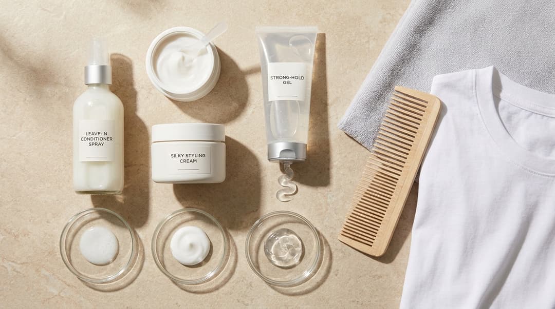 Leave-in conditioner, styling cream, gel, comb, and microfiber towel arranged in a flatlay.