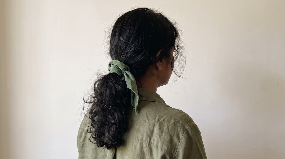 Loose low ponytail secured with a soft fabric tie, shown from behind. AI illustration of a loose hairstyle; comfort and tension depend on how a style is worn.