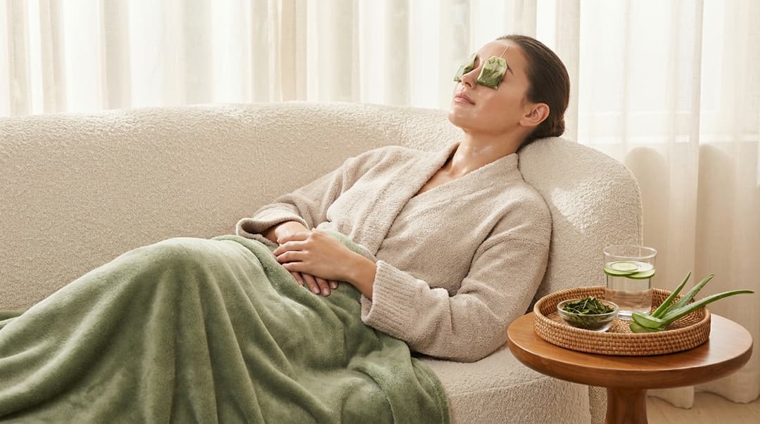 Woman with radiant skin relaxing with chilled green tea bags over her eyes in a spa-like home setting