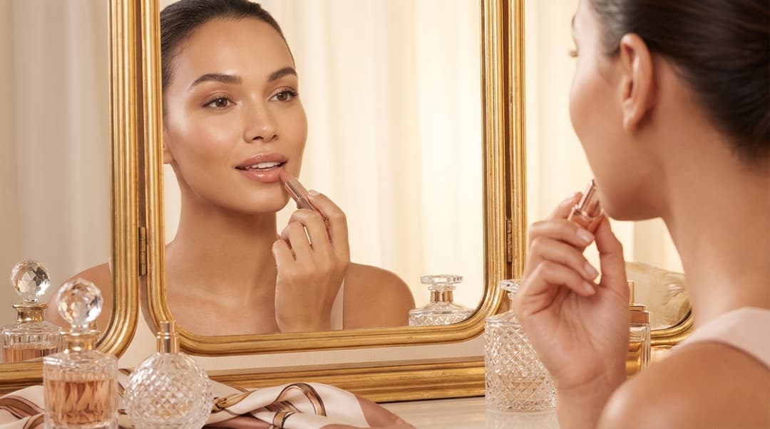 Beautiful woman applying nude glossy lipstick at a vanity mirror