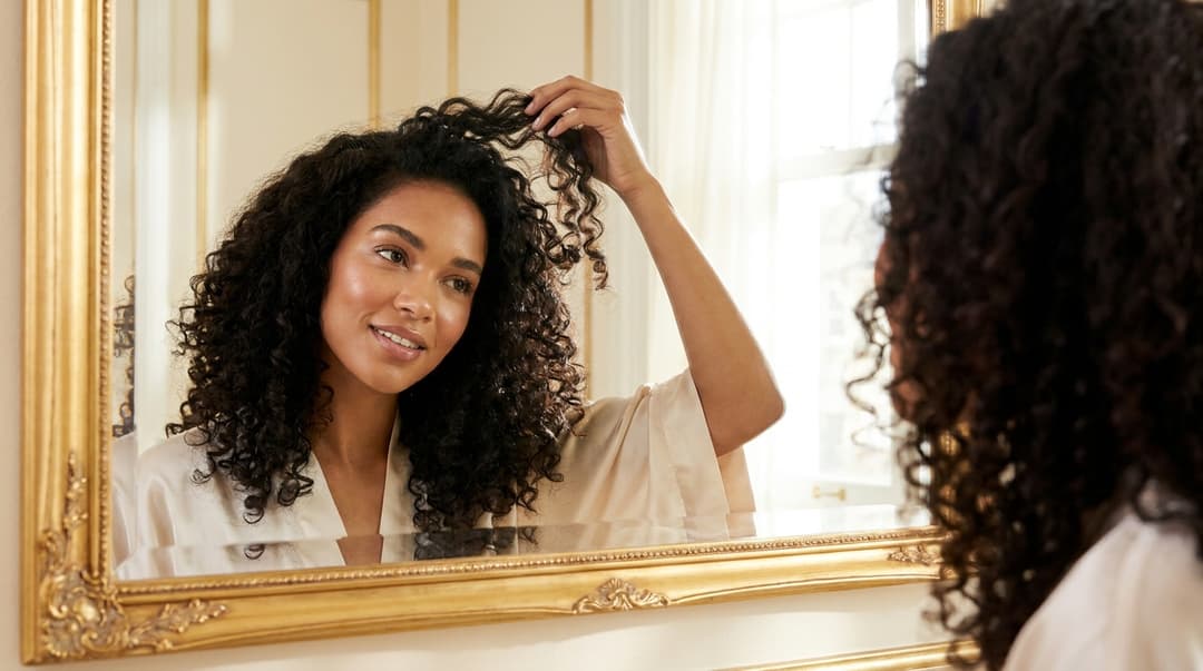 Woman checking the shape and volume of her day-2 curls in a mirror