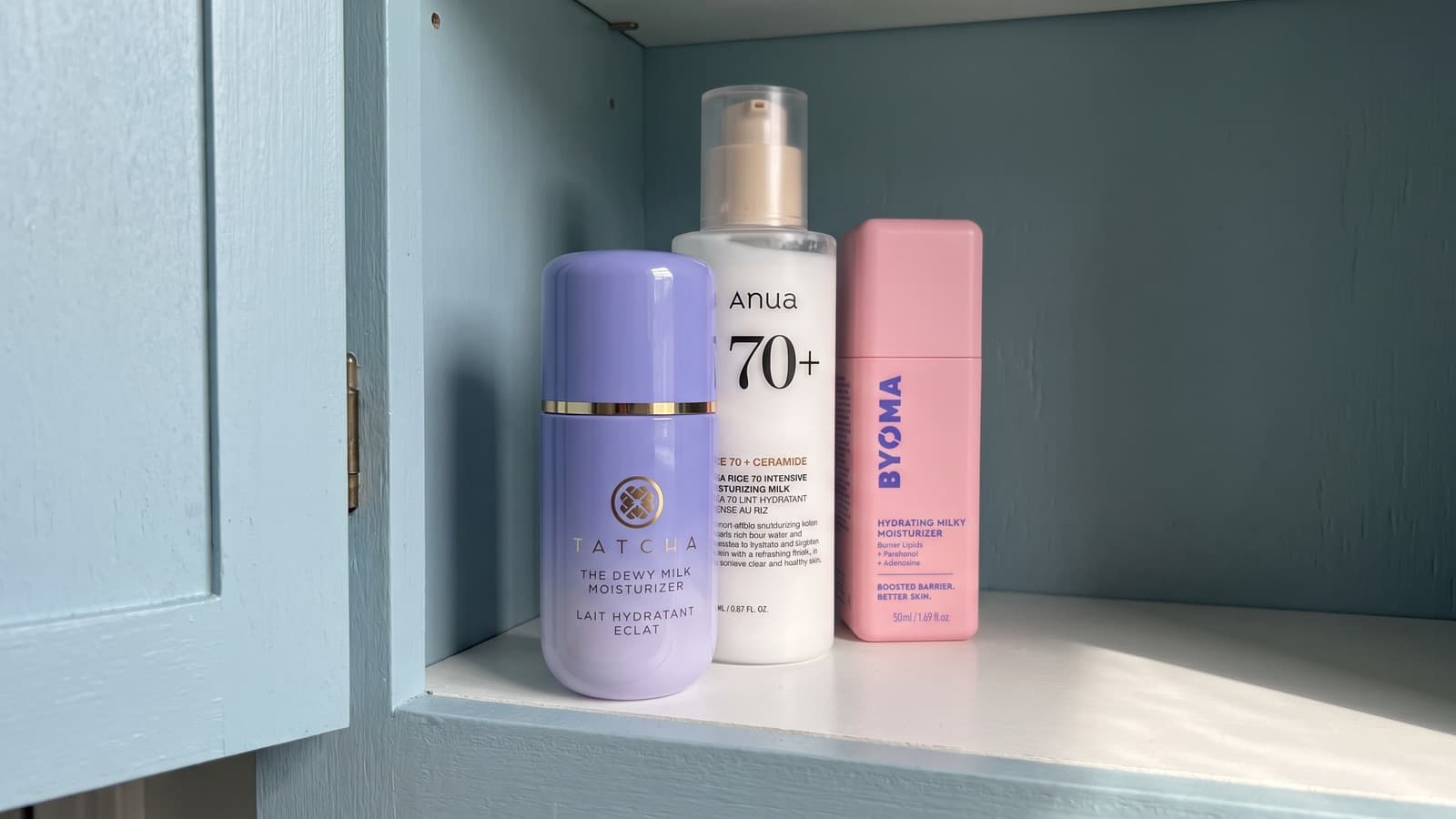 Tatcha Dewy Milk, Anua Rice 70 Milk and BYOMA Milky Moisturizer in a blue cabinet