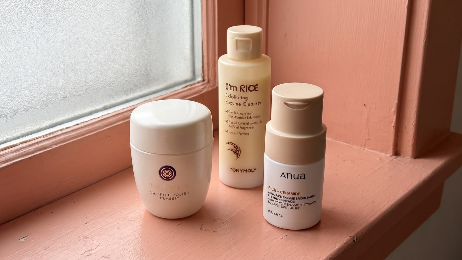 Tatcha Rice Polish Classic, TONYMOLY I’m Rice and Anua cleansing powder on a coral windowsill